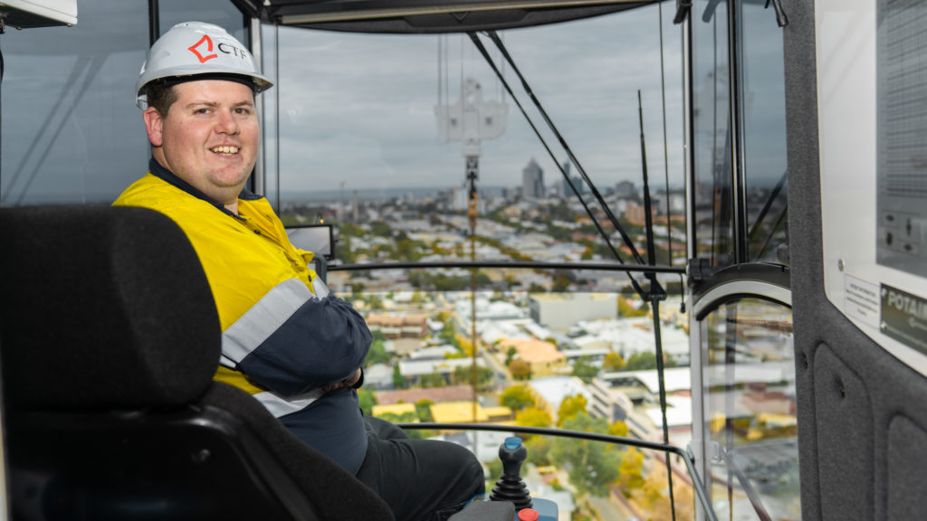 Male crane operator wearing hi-vis and a hard hat sitting in a crane operator's cab